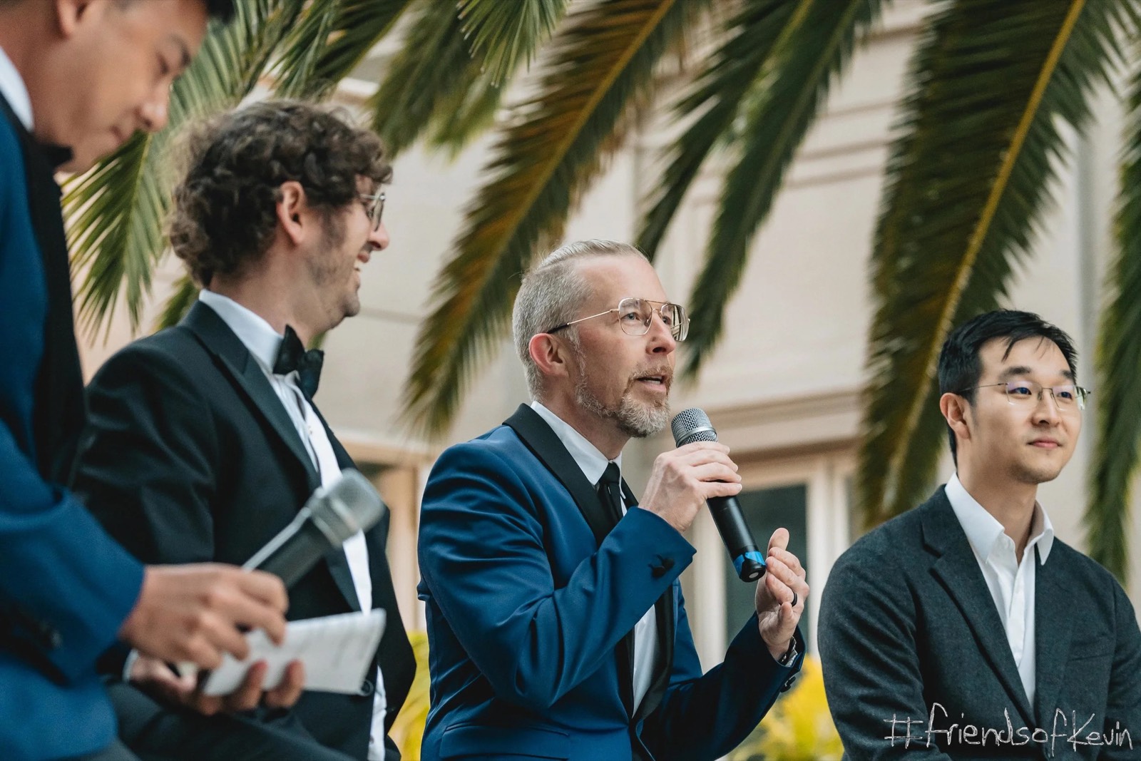 Chris Messina speaking into a microphone on stage, between fellow panelists in suits