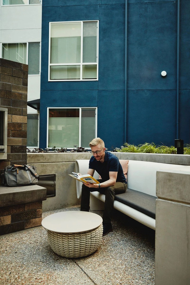 Chris Messina reading a book on a bench in a courtyard